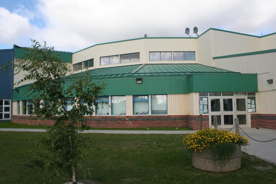 Exterior of Fort Smith recreational facility. The building has a green roof and beige walls. There's a tree and a planter with yellow flowers in the foreground.