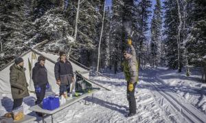 A group of men prepare hot drinks for skiers passing by. 